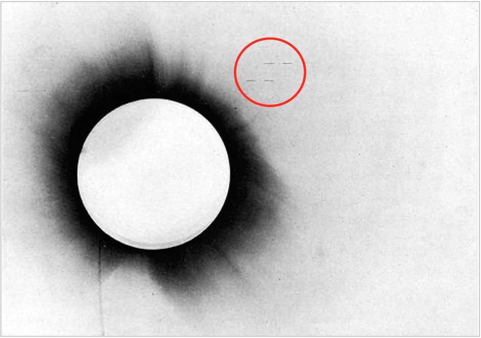 Negative of the 1919 solar eclipse taken from the report of Arthur Eddington. Eddington highlighted the stars he used in the comparison with horizontal marks; these can be seen inside the red circle.